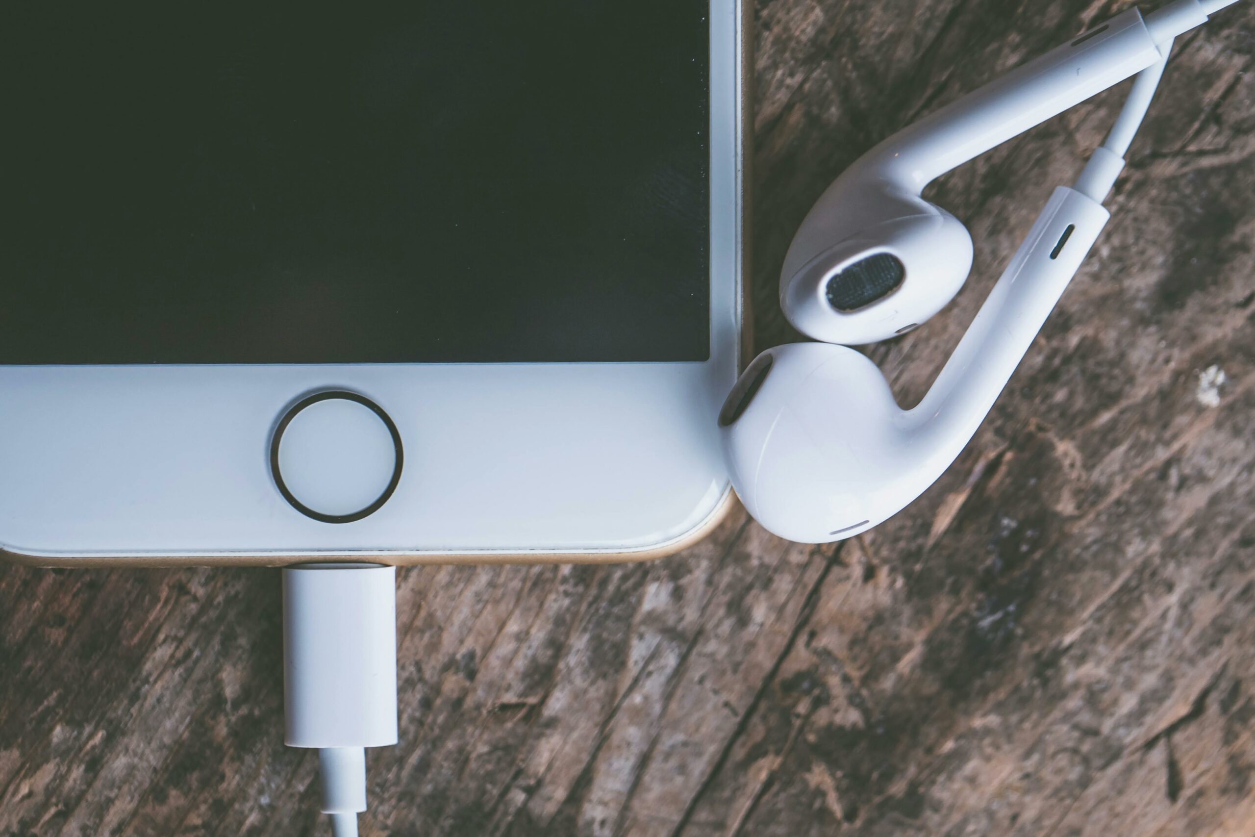 Minimalist close-up of a smartphone with earphones on a rustic wooden surface, highlighting modern technology.